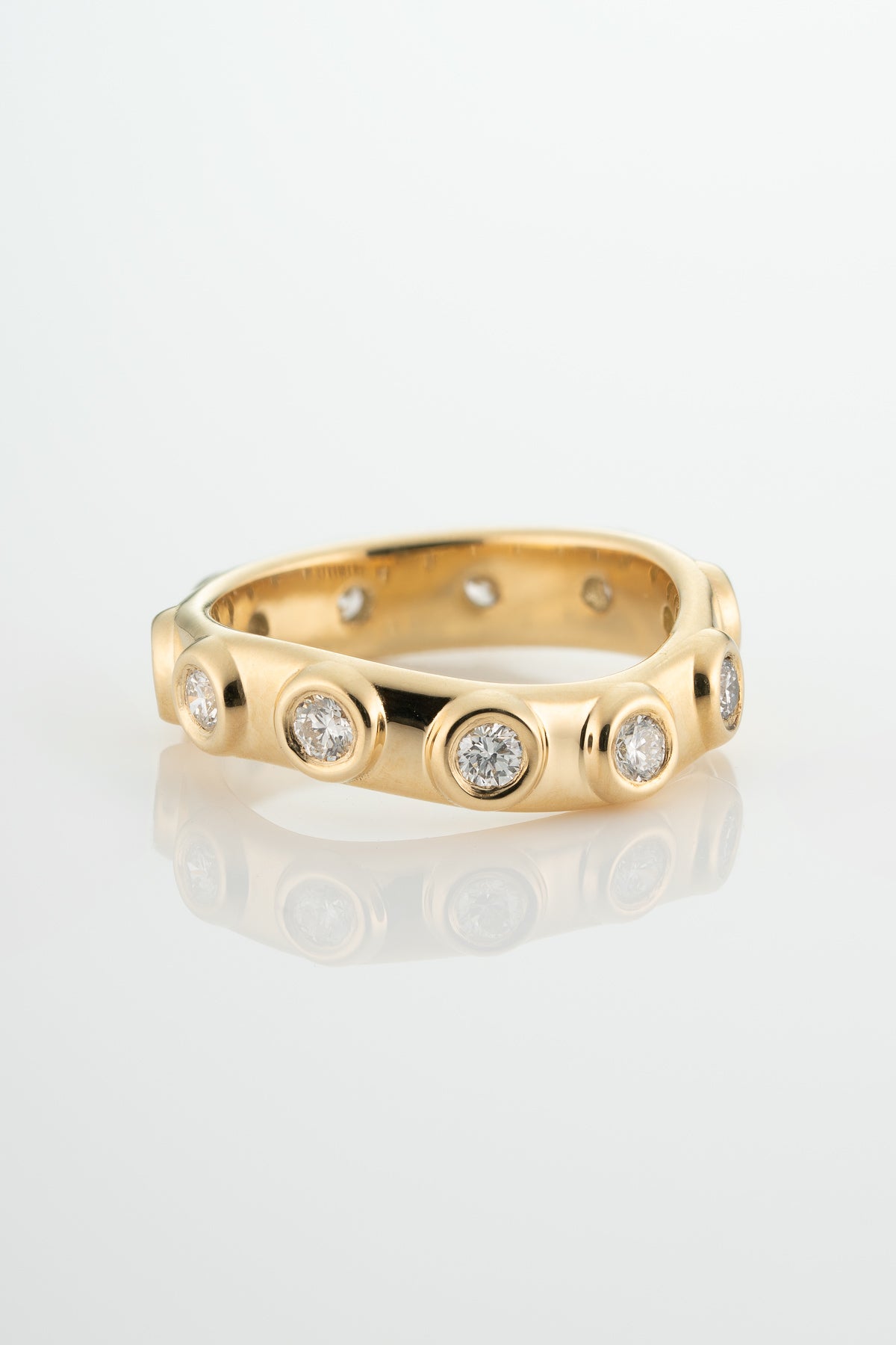 a wide, gold, shaped band with soft chunky bezels surrounding round-cut white diamonds