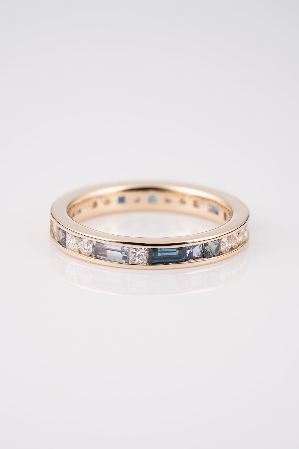 Gold Channel Set Ring with a mixture of white diamond baguettes and rounds, with Australian and Montana Sapphires scattered within the band.