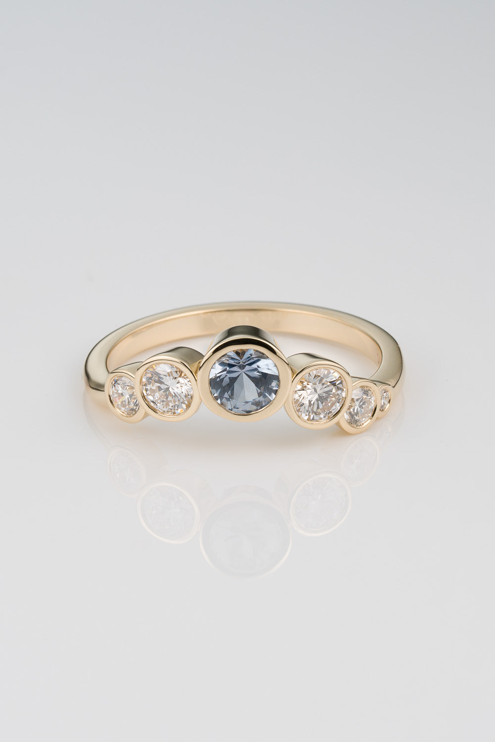 Light Blue Sapphire centerstone ring with graudated diamond detail cascading down the sides in an assymetrical layout.