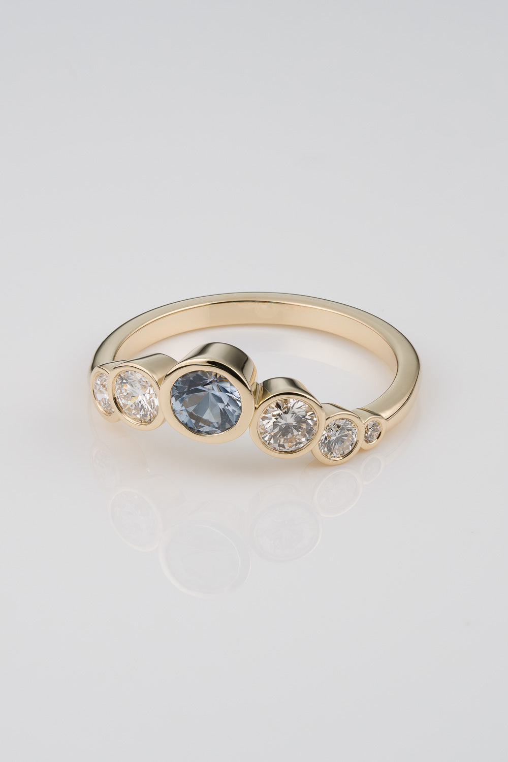 Light Blue Sapphire centerstone ring with graudated diamond detail cascading down the sides in an assymetrical layout.