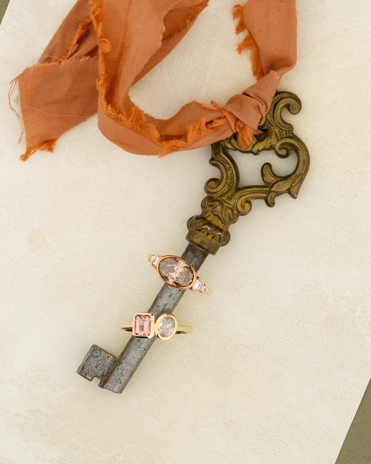 Decorative key with Engagement rings on a white surface with coral ribbon.