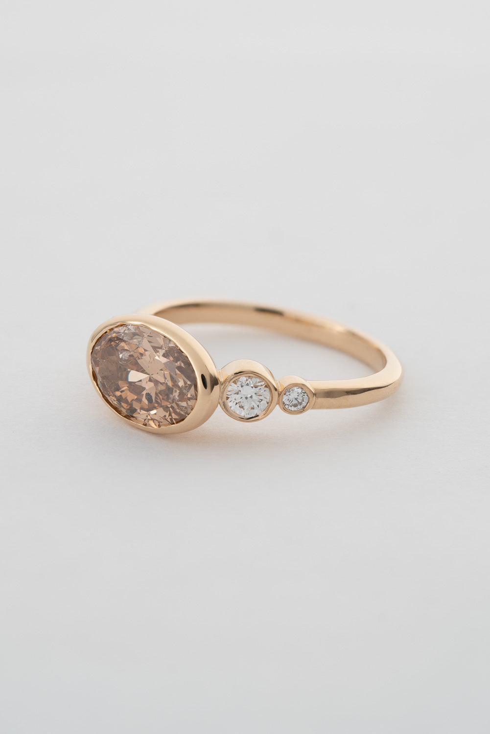 An oval-shaped champagne diamond ring with round white diamonds set in a yellow 14k gold bezel setting with a gold band backing.