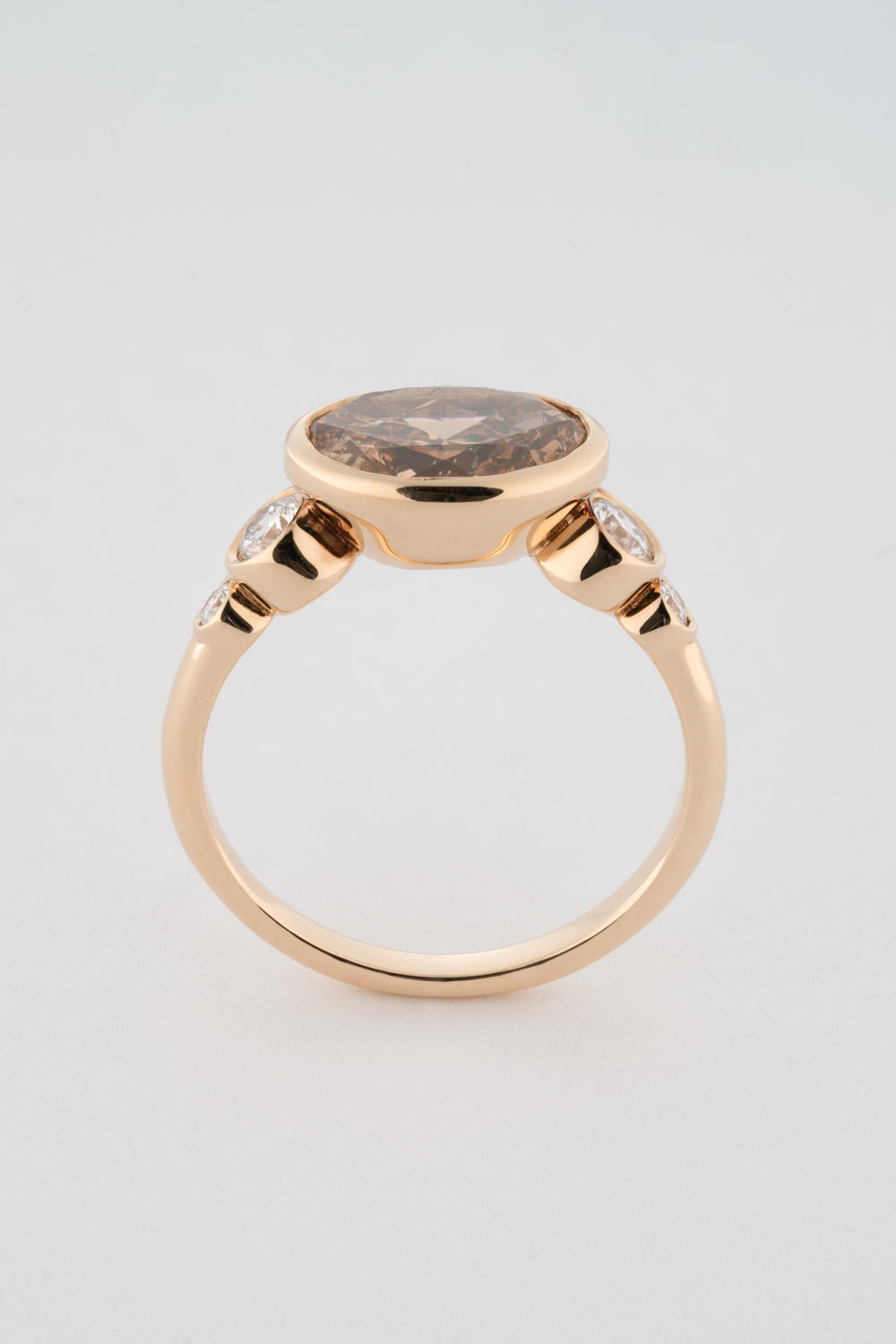 An oval-shaped champagne diamond ring with round white diamonds set in a yellow 14k gold bezel setting with a gold band backing.