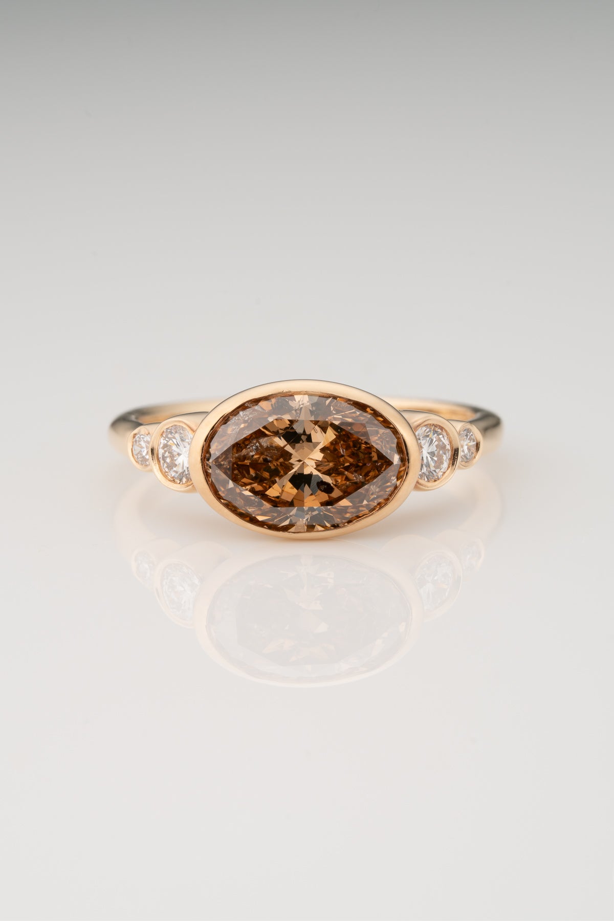 An oval-shaped champagne diamond ring with round white diamonds set in a yellow 14k gold bezel setting with a gold band backing.