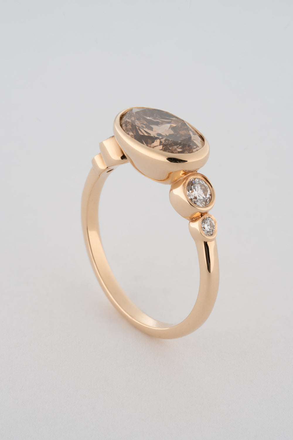 An oval-shaped champagne diamond ring with round white diamonds set in a yellow 14k gold bezel setting with a gold band backing.