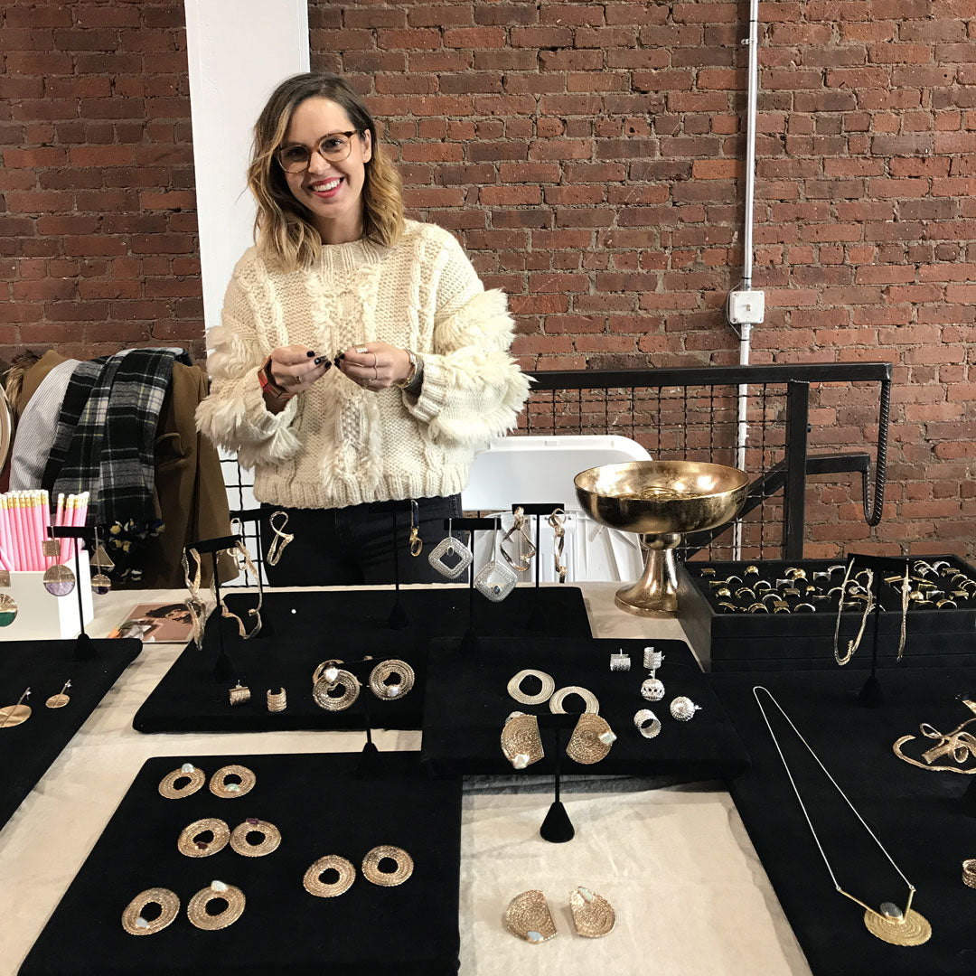 Erica standing behind a table with a collection of gold earrings and necklaces