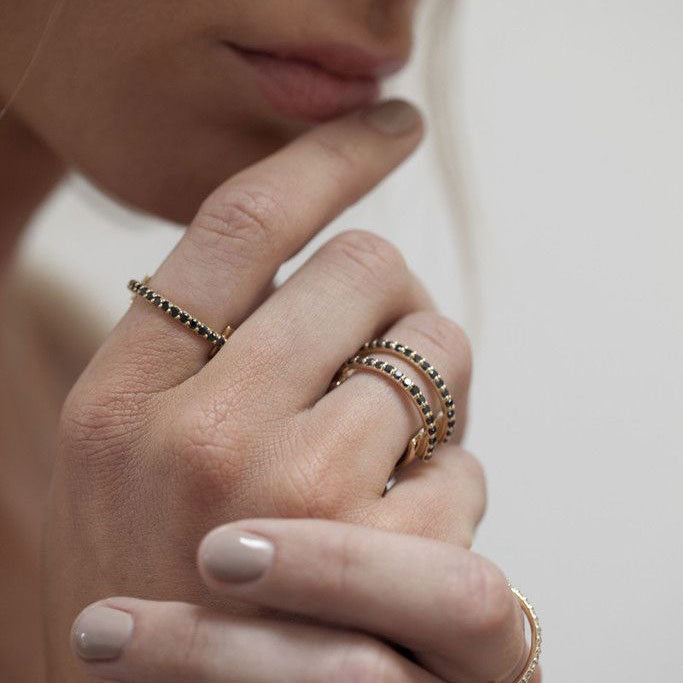 A woman wearing the Anni Ring with black diamonds on her pointer finger and the Double Anni Ring with black diamonds on her ring finger