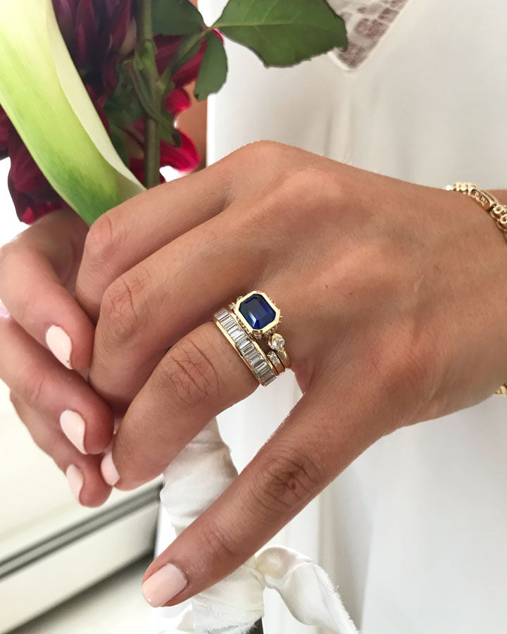 A North South Biggie Baguette Band stacked with a custom ring with a large, navy-colored stone on a woman's hand