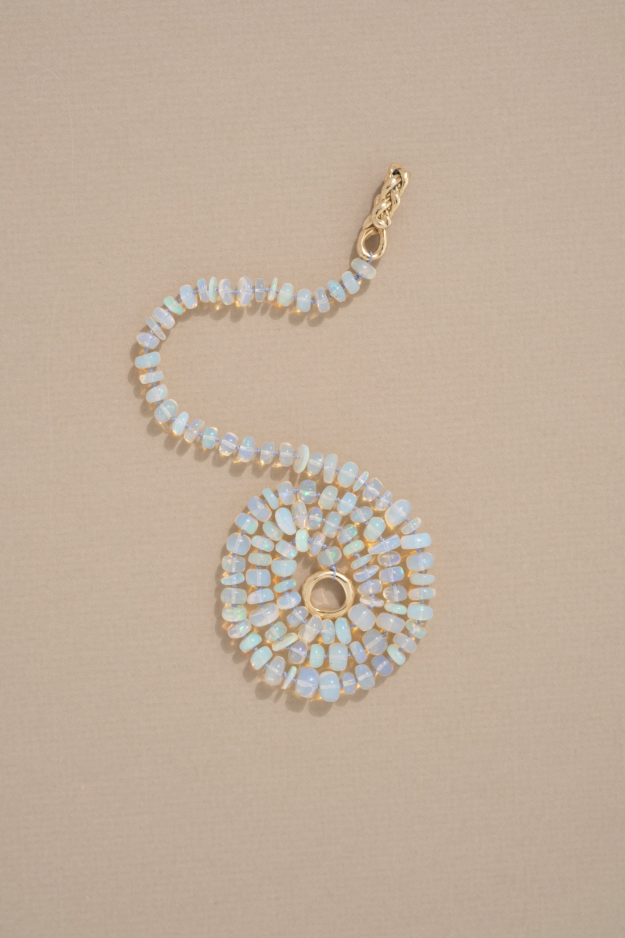 A delicate opal necklace with pearl knotting and a gold braided closure, displayed against a neutral background.