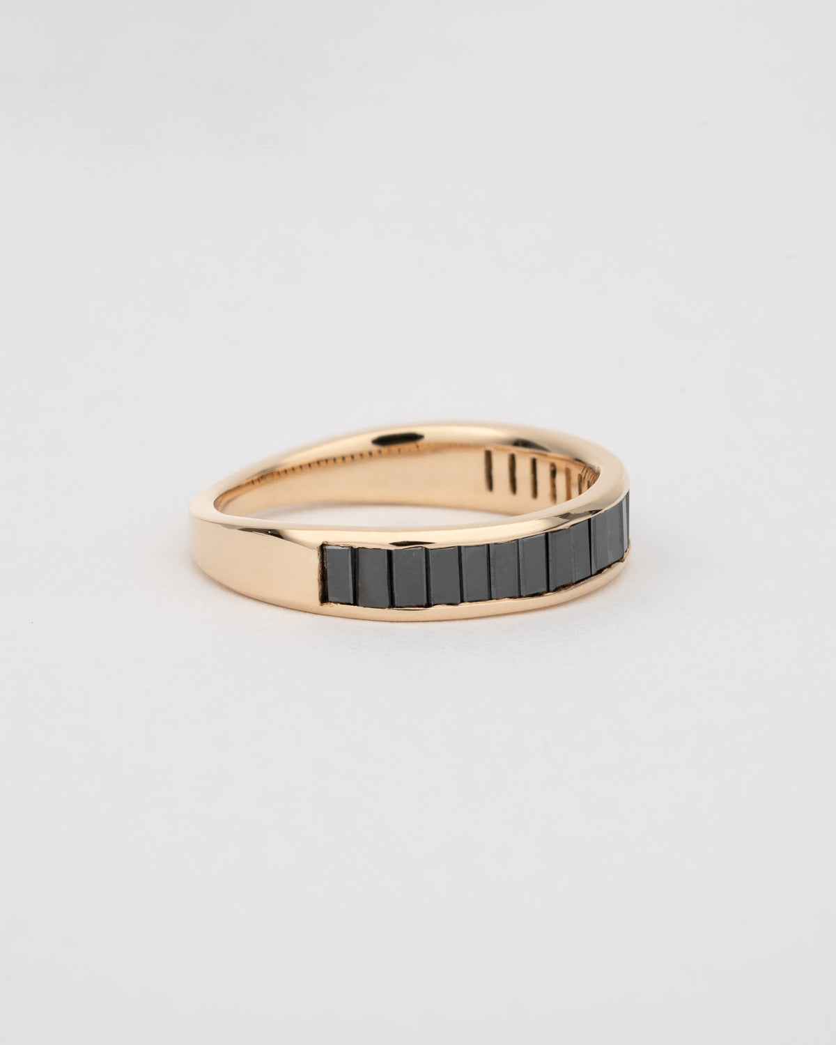 A half eternity ring with channel set black diamond baguettes and a gold tapered backing.