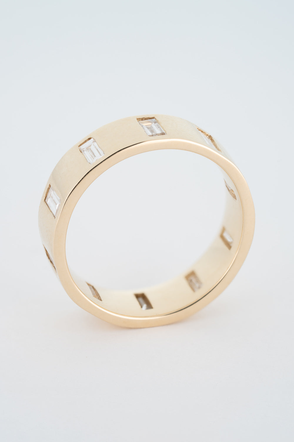 A thick gold band ring with north-south facing baguette cut diamonds gypsy set around its circumference.