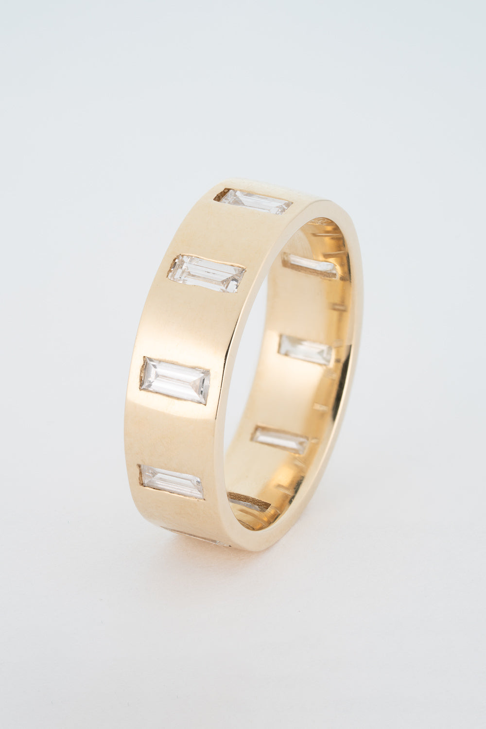 A thick gold band ring with north-south facing baguette cut diamonds gypsy set around its circumference.