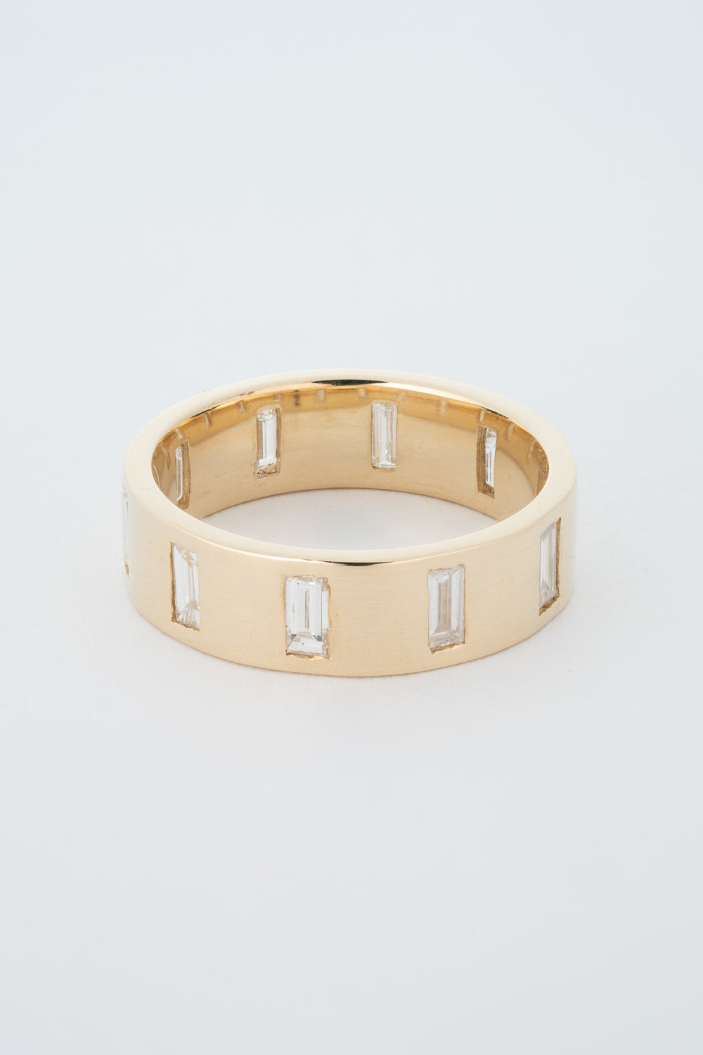 A thick gold band ring with north-south facing baguette cut diamonds gypsy set around its circumference.