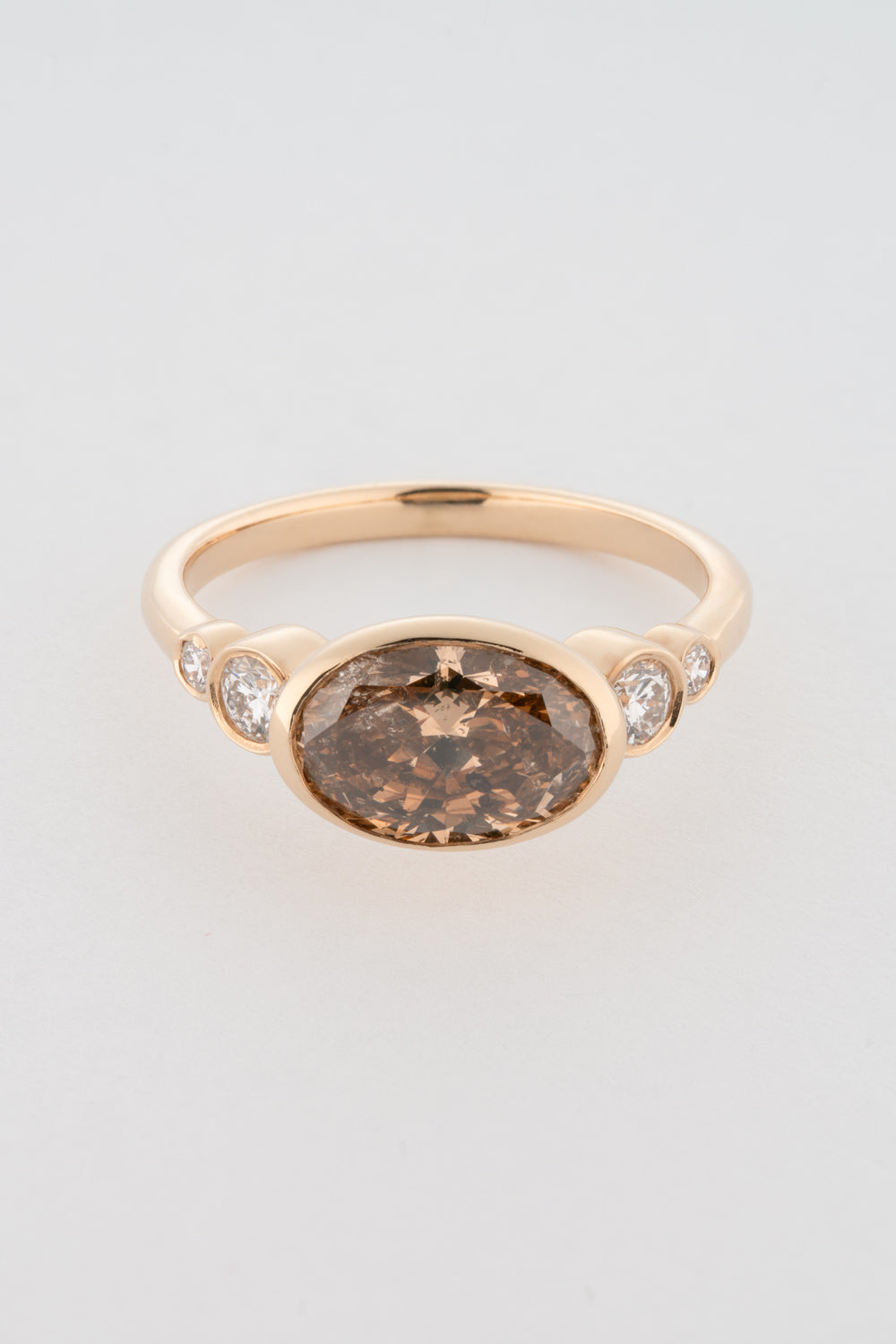 An oval-shaped champagne diamond ring with round white diamonds set in a yellow 14k gold bezel setting with a gold band backing.