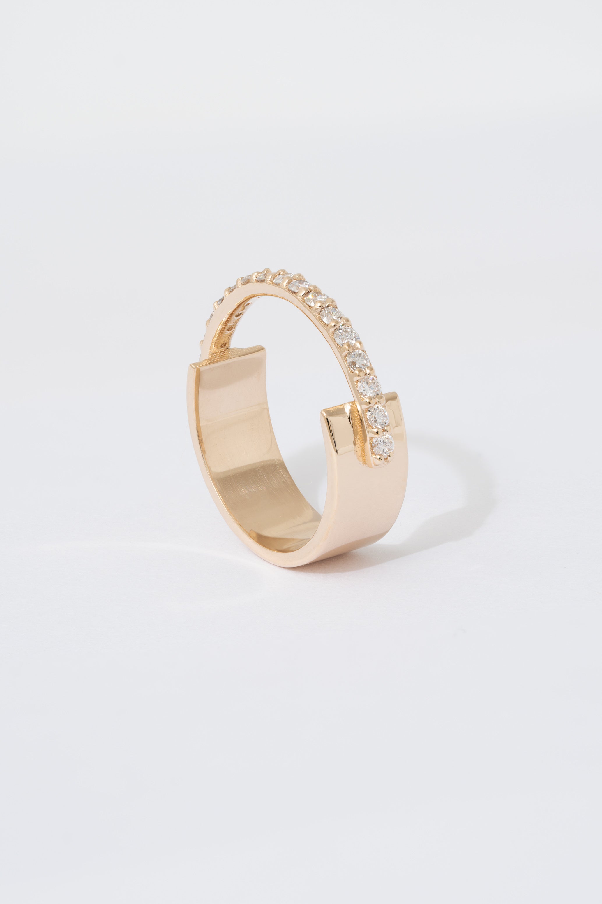 A gold ring with a flat wide backing and a single row of pave white diamonds around the front half of the band, displayed against a white background.