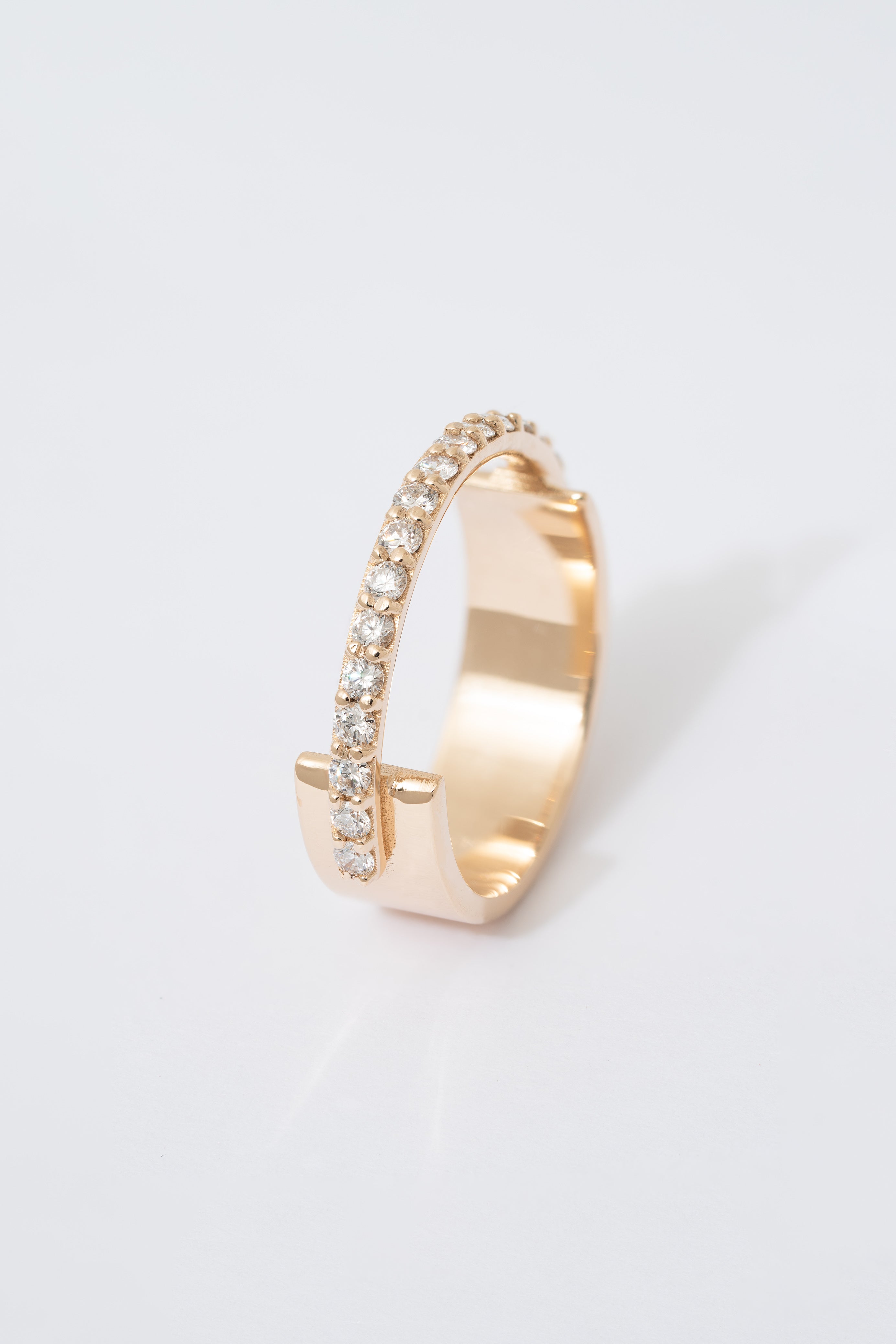 A gold ring with a flat wide backing and a single row of pave white diamonds around the front half of the band, displayed against a white background.