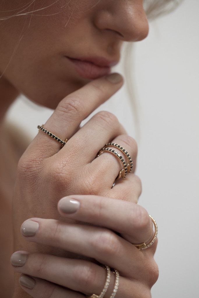 A large gold ring with a flat cigar backing design featuring two rows of pave black diamonds in the front of the ring shown on a model. 