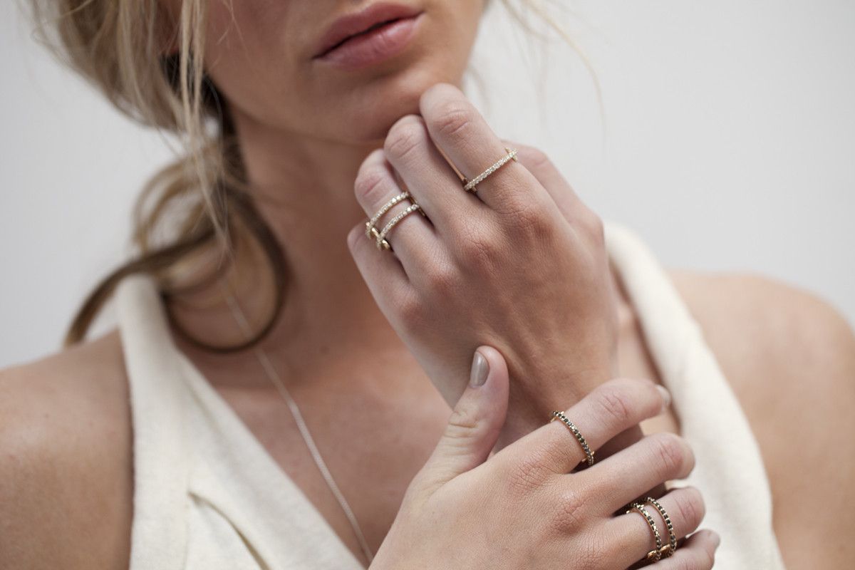 A large gold ring with a flat cigar backing design featuring two rows of pave black diamonds in the front of the ring shown on a model. 