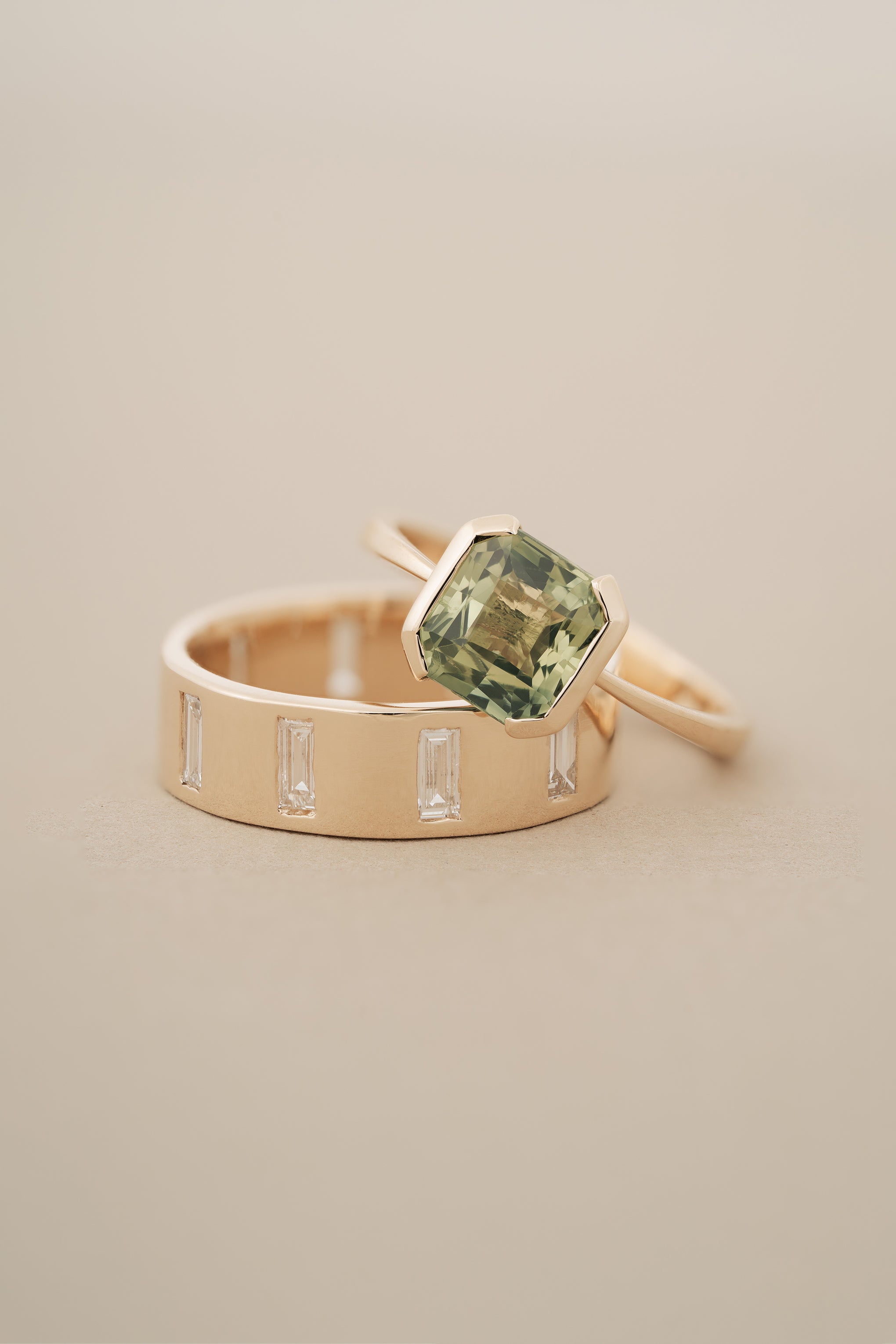 A thick gold band ring with north-south facing baguette cut diamonds gypsy set around its circumference, with a Split Bezel Green Sapphire Solitaire