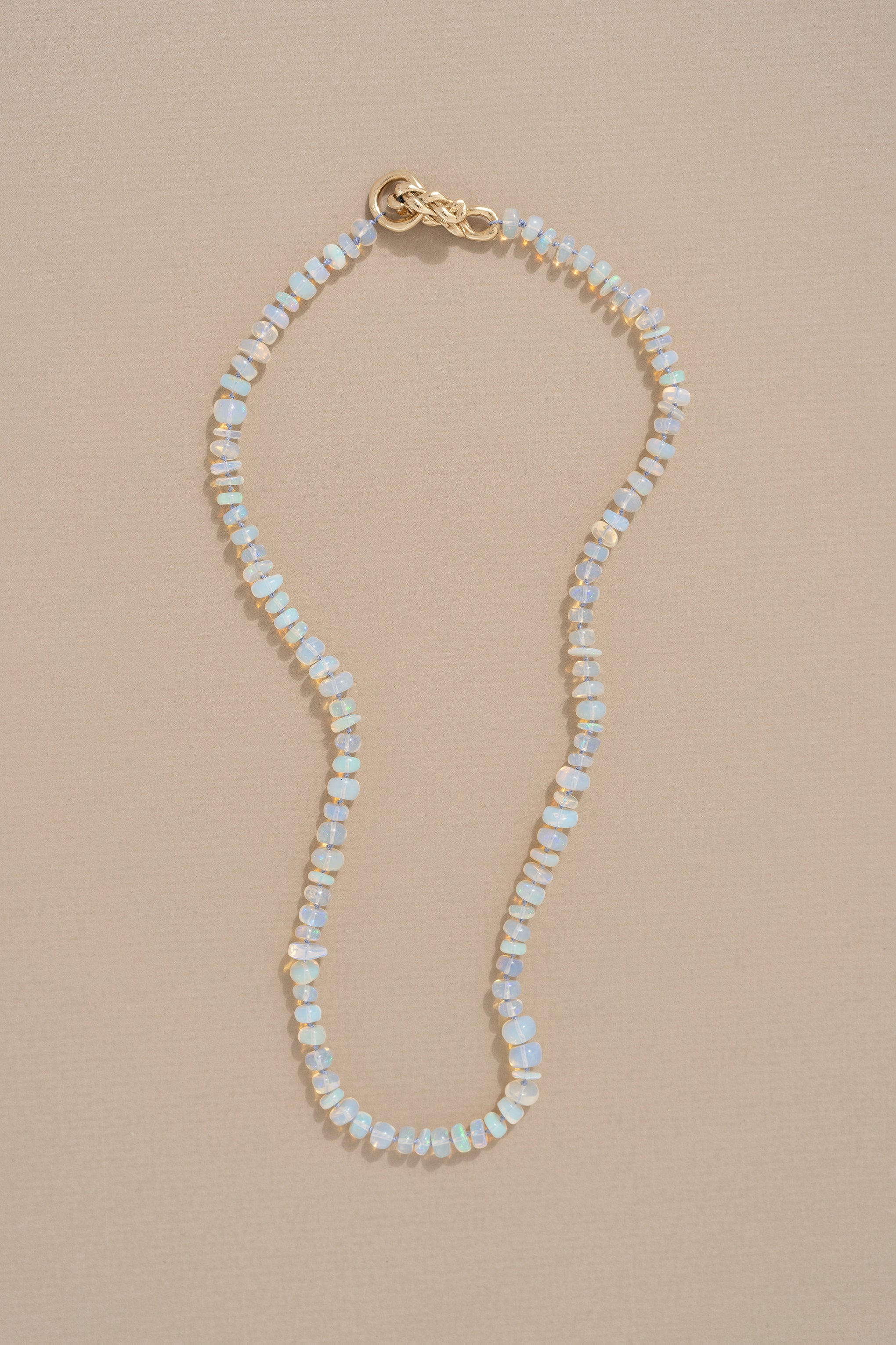 A delicate opal necklace with pearl knotting and a gold braided closure, displayed against a neutral background.