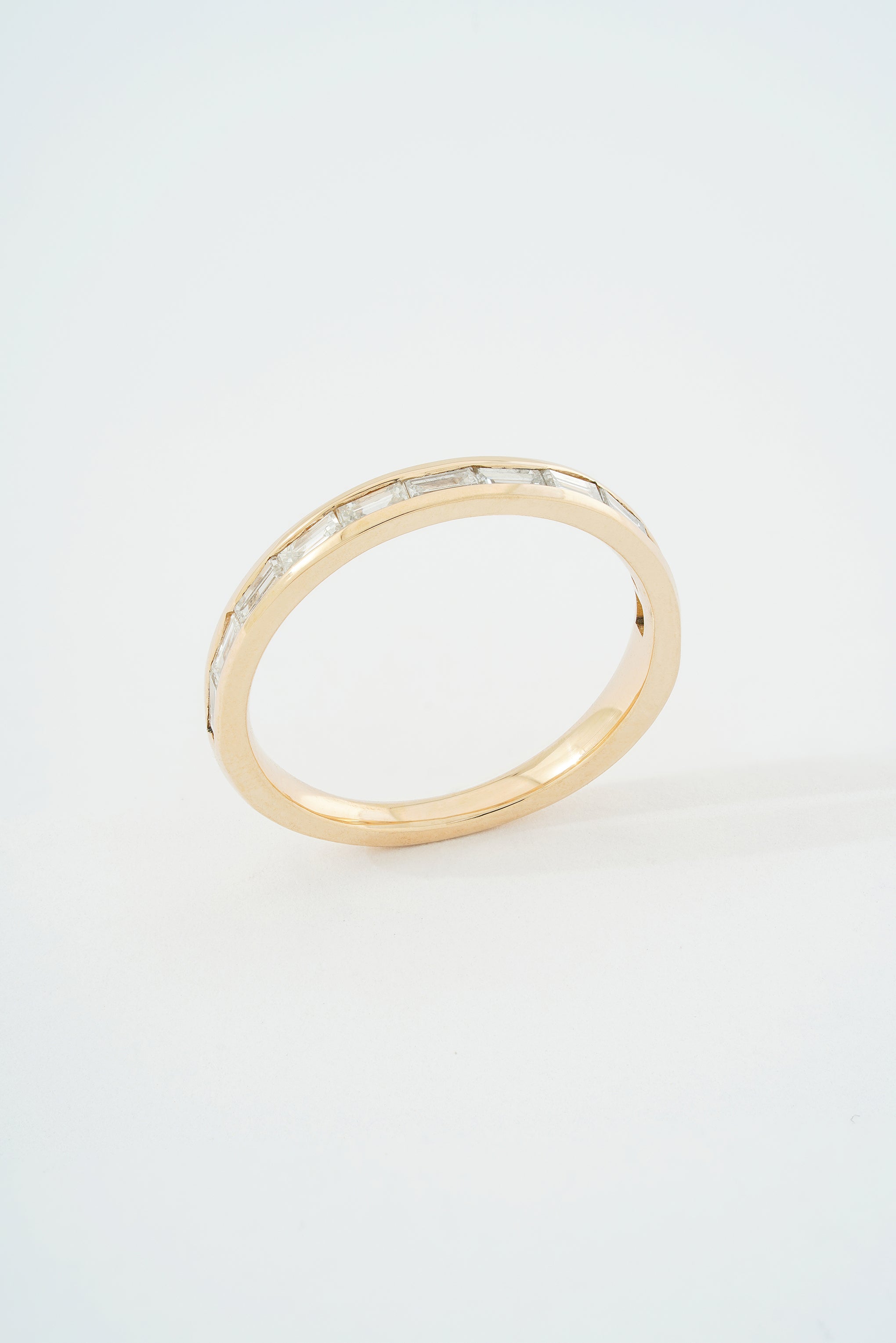 A gold half eternity band ring with channel set baguette cut diamonds, featuring a tapered design and slightly rounded profile.